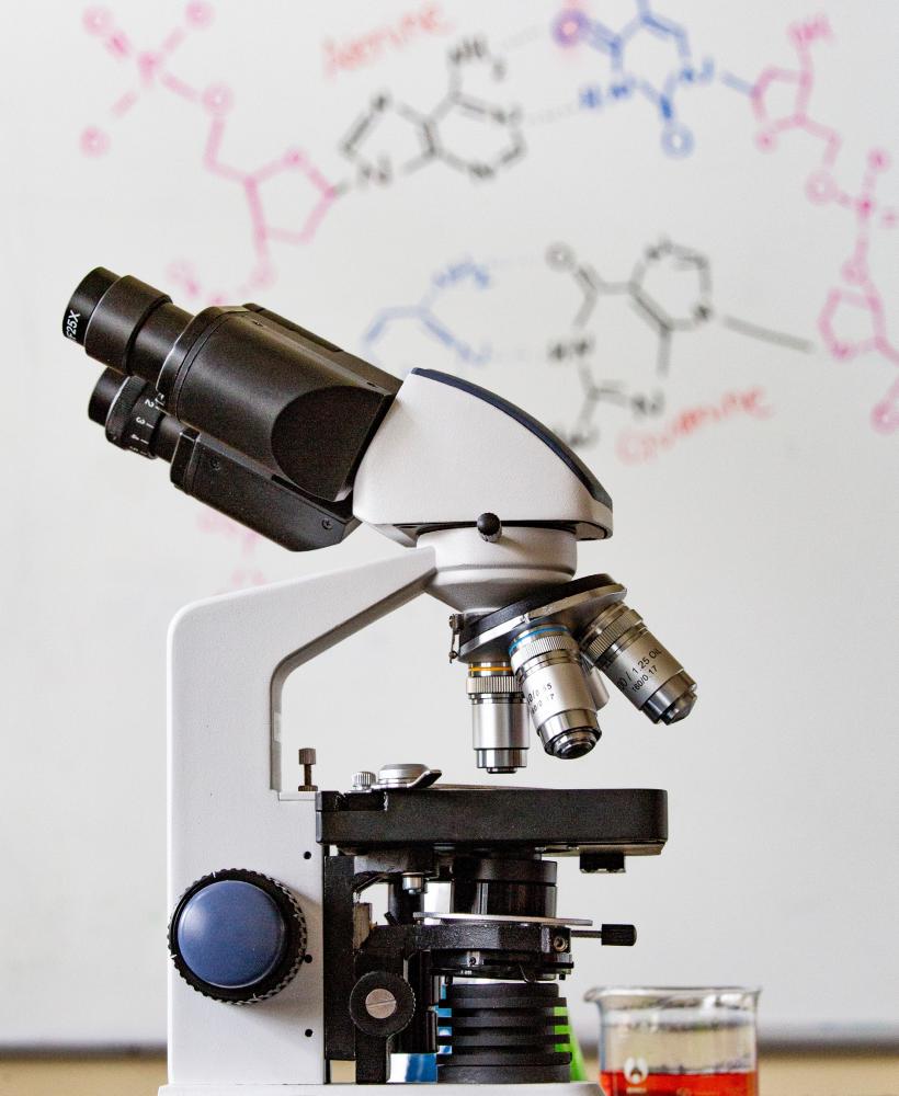 A microscope sits in front of a whiteboard with molecular formulas written on it in various colors of ink. 