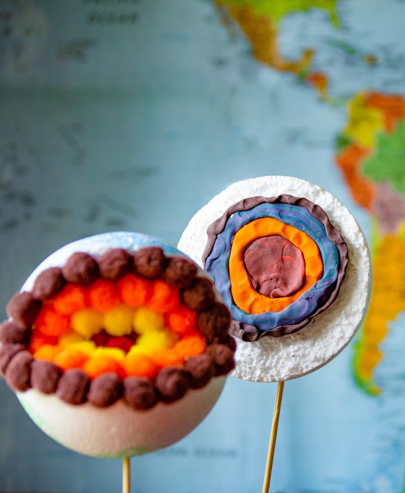 A set of hand-made clay models demonstrating the layers of the earth, sitting in front of a map of the world. 